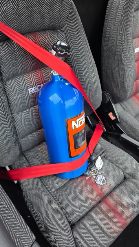 Cilindro de nitro NOS preso ao banco Recaro com cinto vermelho